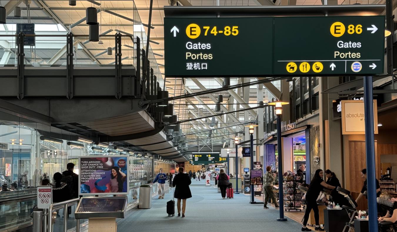 A walkway in an airport with a large sign overhead indicating the direction of the gates