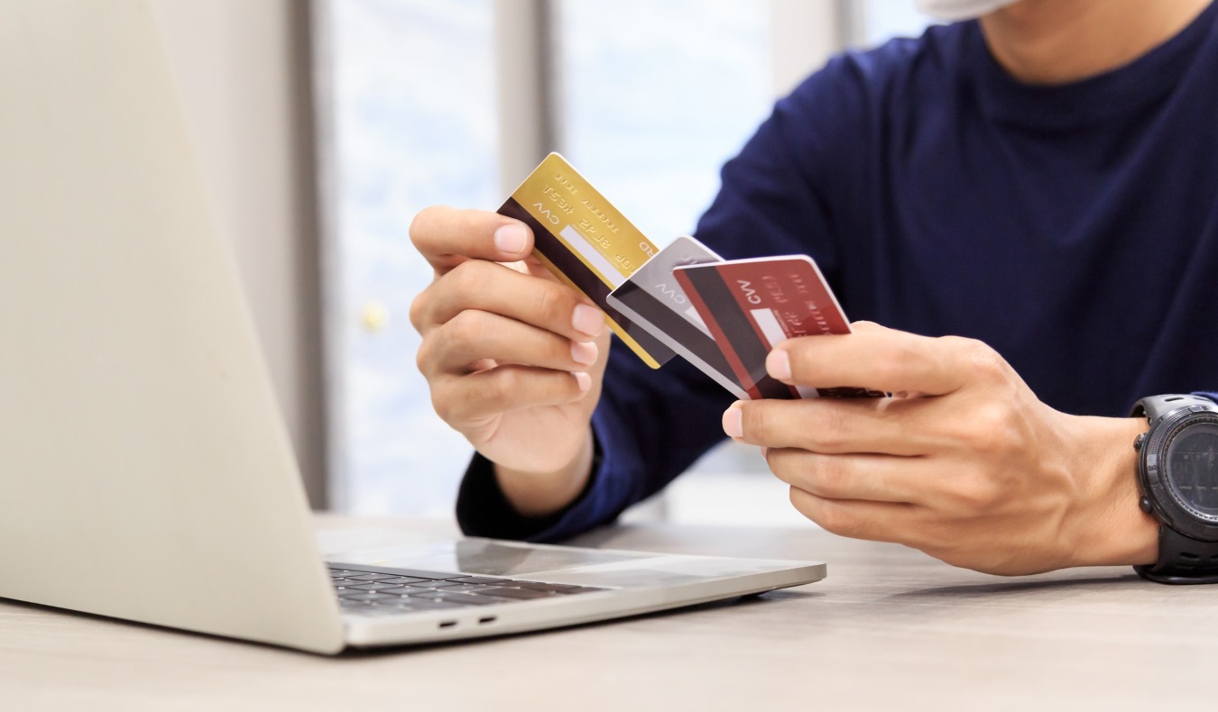 A man sitting in front of a laptop holding a few credit cards in his hand