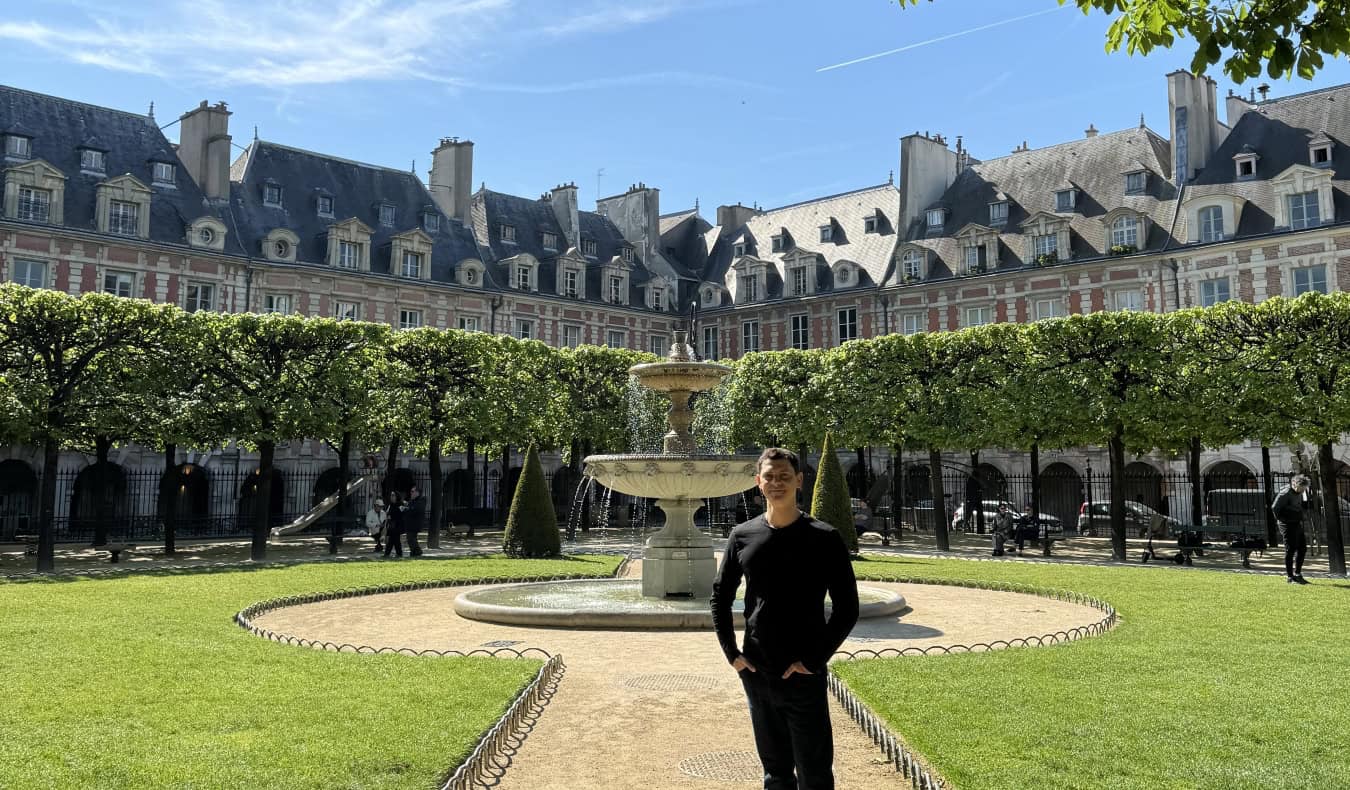 Nomadic Matt standing in the Place de Vosages, a large enclosed square surrounded by buildings, with a fountain in the middle, in Paris, France