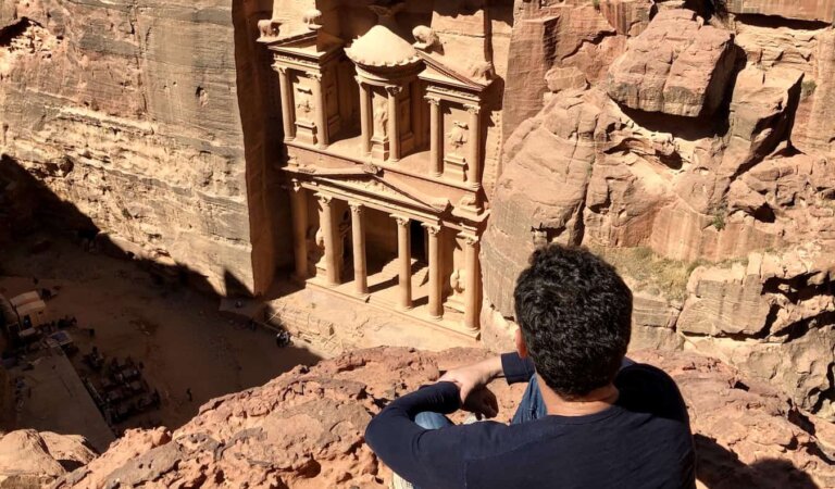 Nomadic Matt posing on a cliff looking out over Petra in Jordan